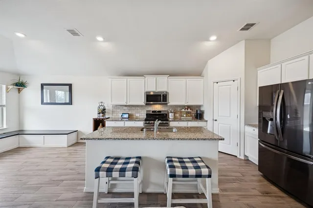 a kitchen with stainless steel appliances granite countertop a dining table chairs refrigerator and microwave