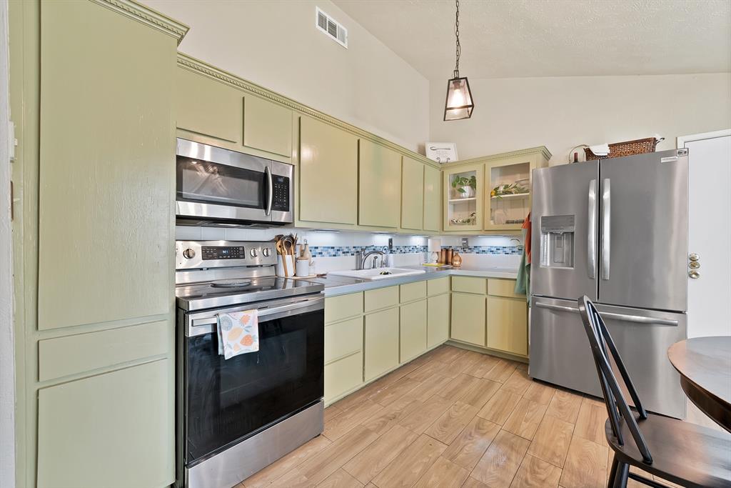 9519 County View Road Dallas, TX 75249 - Photo 8 of 31 Kitchen featuring light green cabinetry, stainless steel appliances, wood-finish flooring, and a tiled backsplash