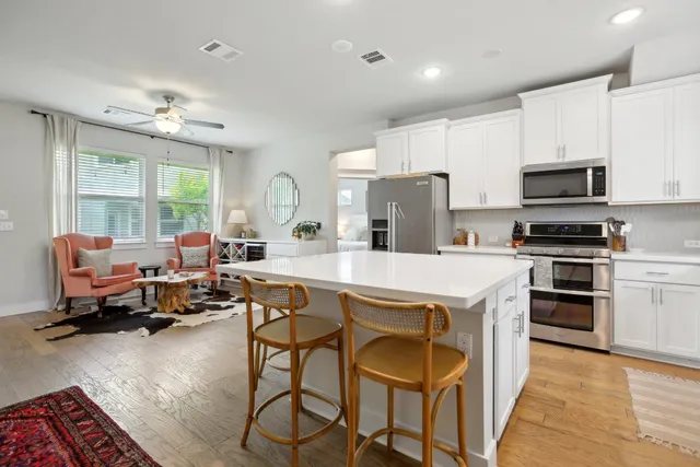 a kitchen with stainless steel appliances a stove a sink a refrigerator white cabinets and couches with wooden floor