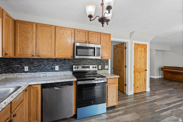 1346 Archmore Drive Springville, UT 84663 - Photo 2 of 32 Kitchen featuring wood cabinetry, dark stone-look backsplash, light-colored countertops, and stainless steel appliances including an oven range, microwave, and dishwasher
