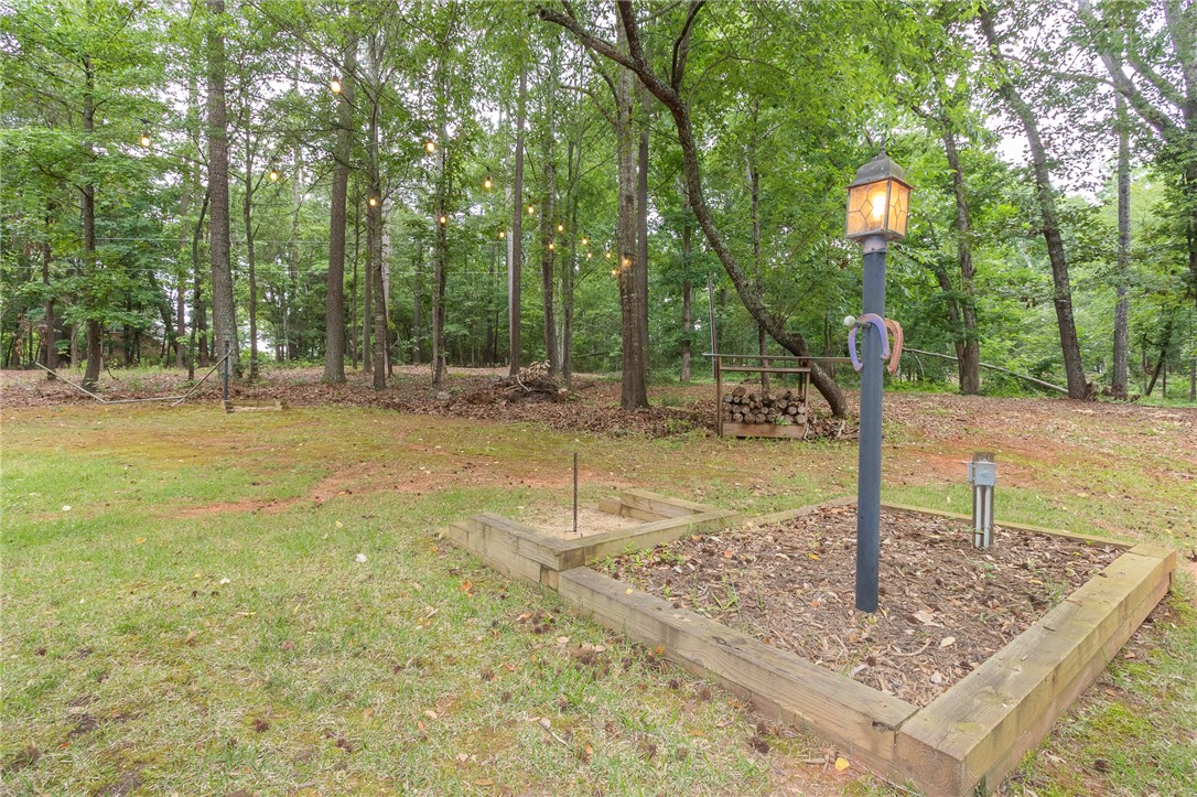 203 Oak Hollow Pendleton, SC 29670 - Photo 45 of 50 Backyard retreat featuring a horseshoe pit and string lights, surrounded by a peaceful wooded landscape.