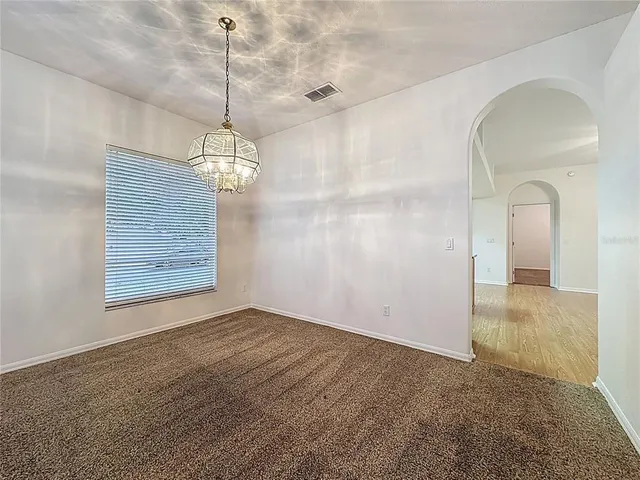 a view of an empty room and kitchen with wooden floor