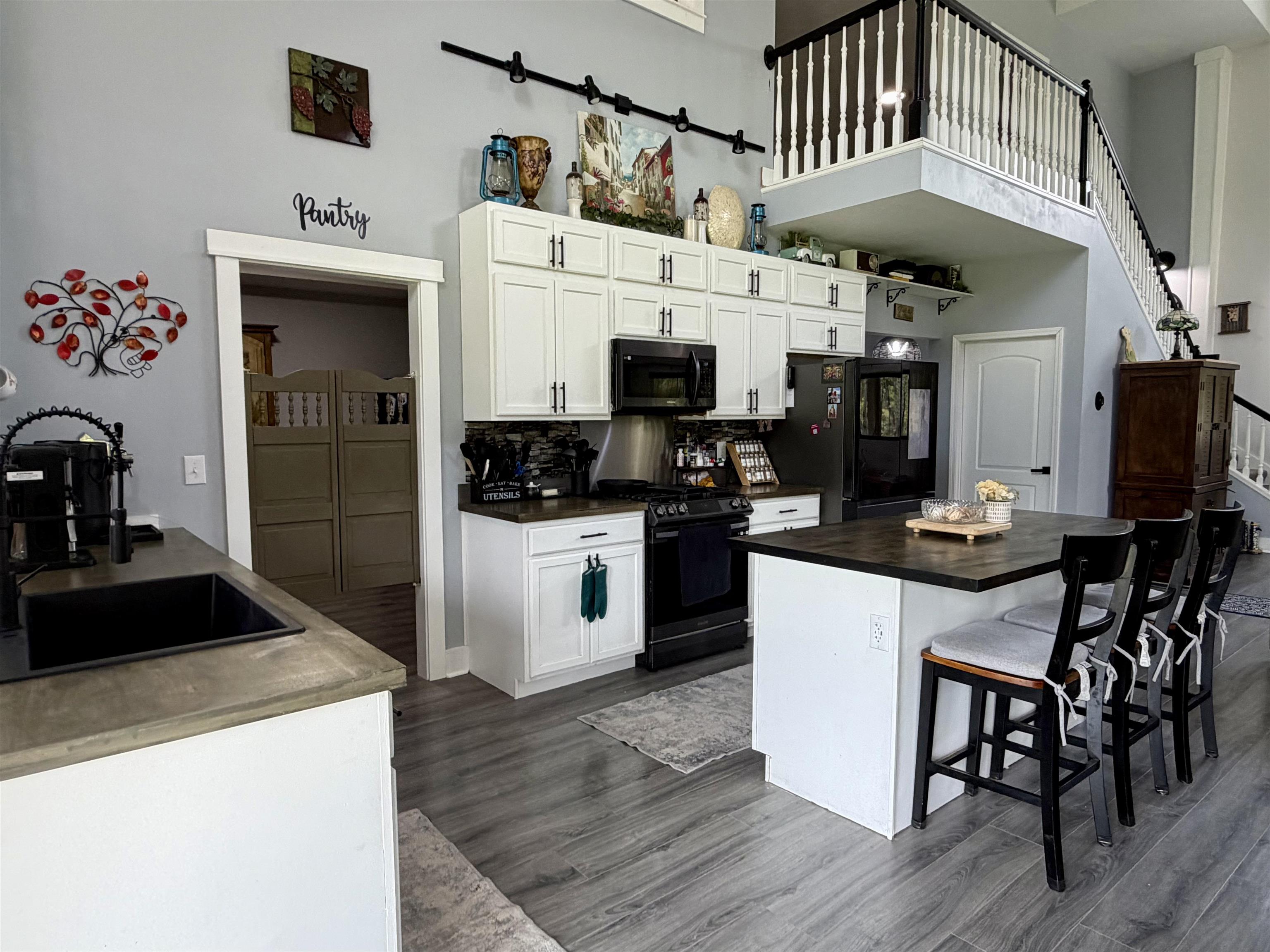 3670 Peavine Road Middleton, TN 38052 - Photo 7 of 36 Kitchen with white cabinetry, black appliances, a central island with seating, wood-finish flooring, and a visible pantry entrance