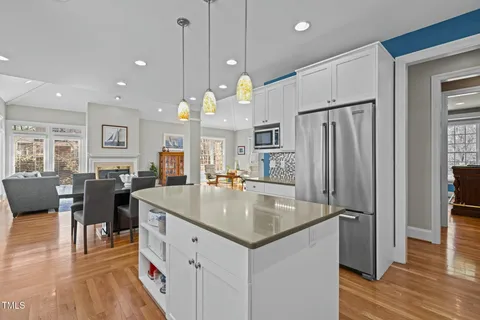 a kitchen with stainless steel appliances granite countertop a refrigerator a sink dishwasher a oven and a dining table with wooden floor