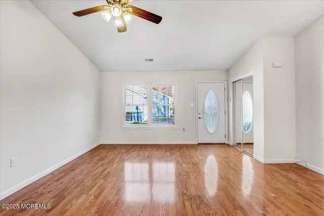 an empty room with wooden floor chandelier fan and windows