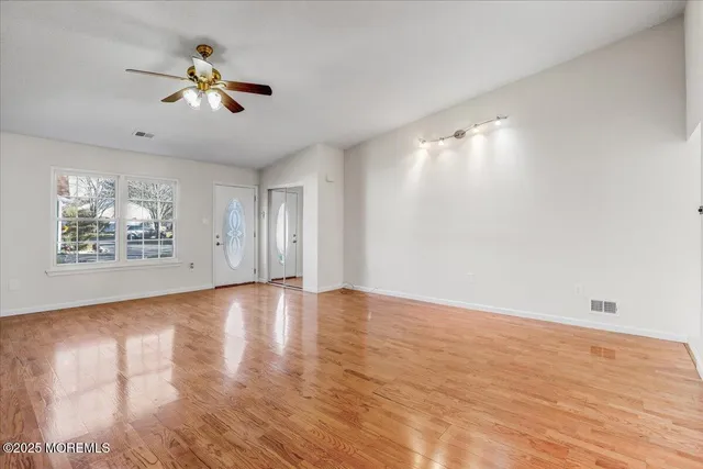 an empty room with wooden floor chandelier fan and windows