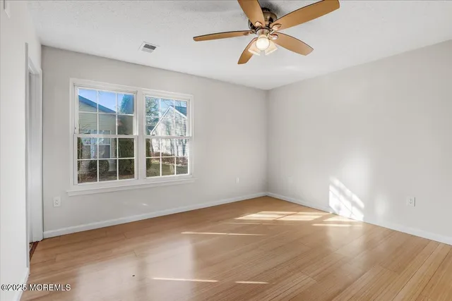 an empty room with wooden floor fan and windows