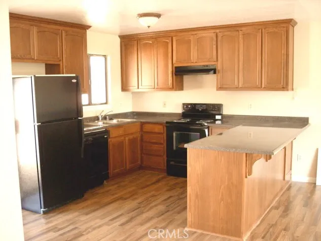 a kitchen with stainless steel appliances granite countertop a refrigerator a sink dishwasher and wooden cabinets with wooden floor