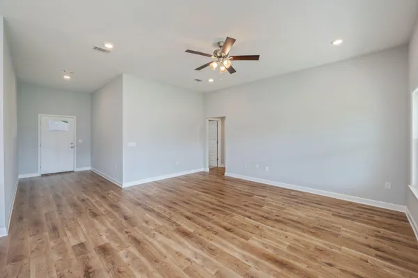 a view of an empty room with wooden floor and a ceiling fan
