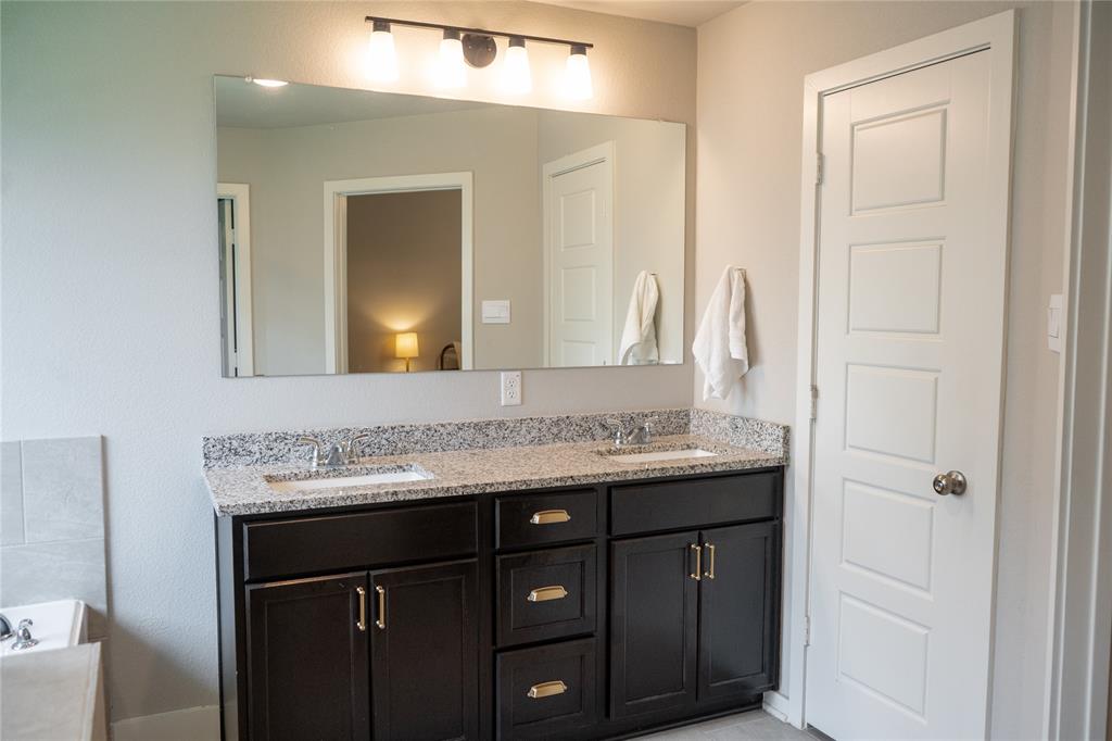 7909 Townsend Drive Waco, TX 76708 - Photo 11 of 22 Dual vanity with dark wood cabinetry, brass hardware, and a speckled countertop