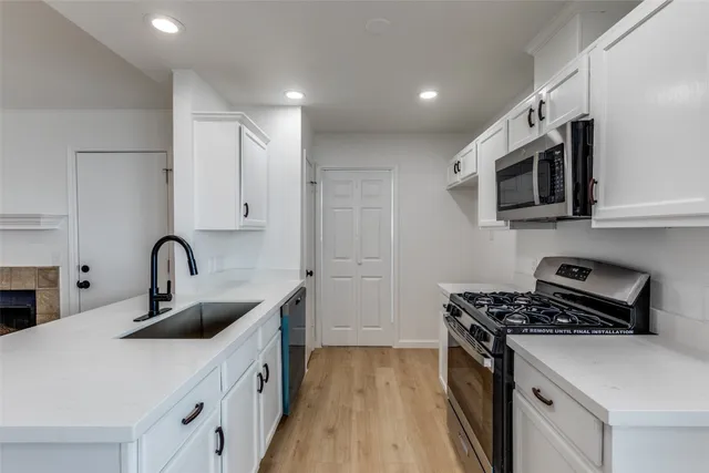 a kitchen with stainless steel appliances a sink dishwasher stove and microwave with wooden floor