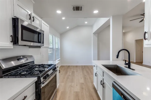 a kitchen with stainless steel appliances a sink a stove top oven a sink dishwasher and white cabinets with wooden floor