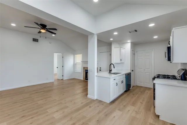 a large white kitchen with a stove a sink dishwasher and a refrigerator with wooden floor