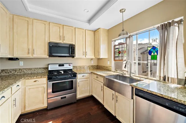 a kitchen with stainless steel appliances granite countertop a sink a stove a refrigerator cabinets and a window