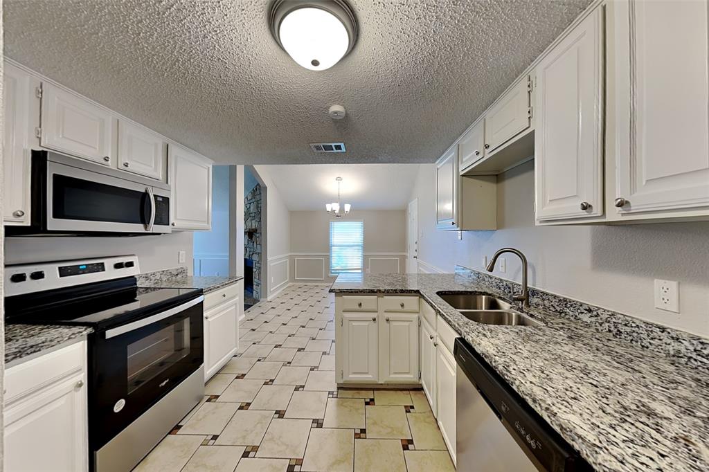 Kitchen featuring stainless steel appliances, light stone countertops, wainscoting, a chandelier, and decorative light fixtures