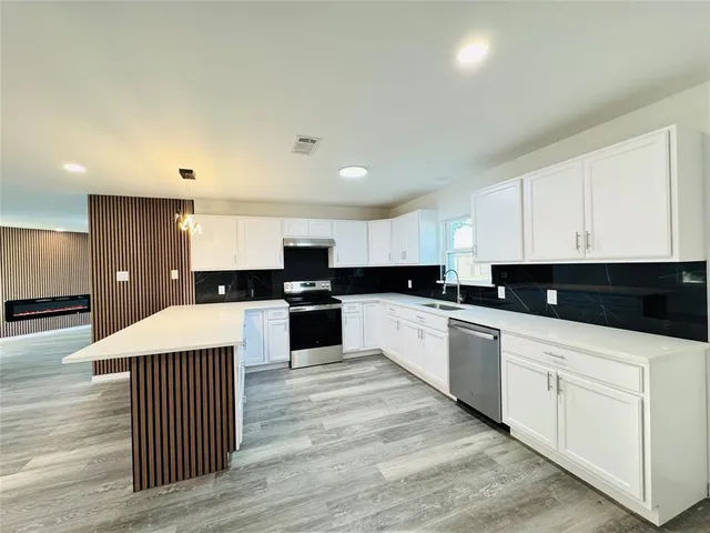 a large kitchen with kitchen island a sink dishwasher a stove and white cabinets with wooden floor