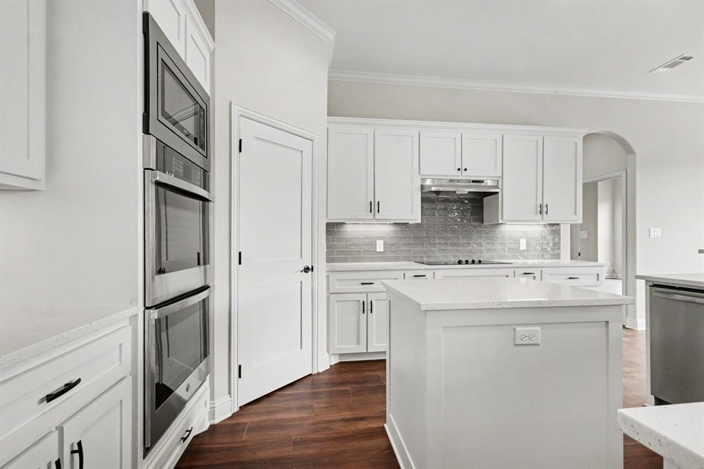 530 P R 491 Leonard, TX 75452 - Photo 14 of 35 Modern kitchen featuring white shaker cabinetry, stainless steel built-in appliances, a central island with a solid surface countertop, wood-finish flooring, and subway tile backsplash