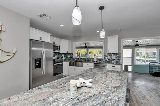 a kitchen with stainless steel appliances kitchen island granite countertop a refrigerator oven a sink dishwasher a dining table and chairs with wooden floor