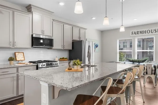 a kitchen with stainless steel appliances granite countertop a stove a sink a microwave a refrigerator and white cabinets with wooden floor