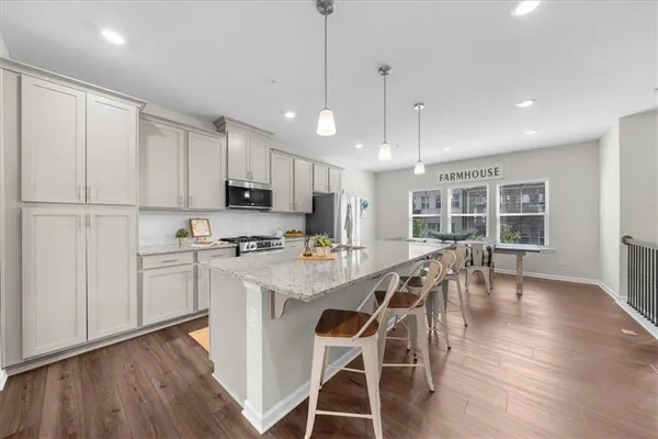 a kitchen with stainless steel appliances granite countertop a stove a refrigerator a microwave oven a sink with island and chairs with wooden floor