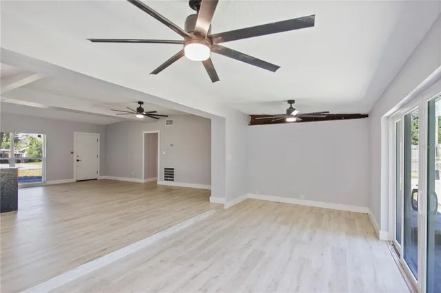 an empty room with wooden floor fan and windows