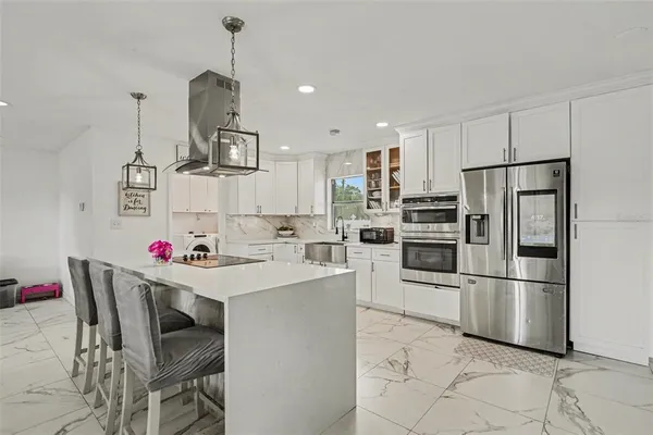 a kitchen with stainless steel appliances kitchen island granite countertop a refrigerator a stove and white cabinets with wooden floor