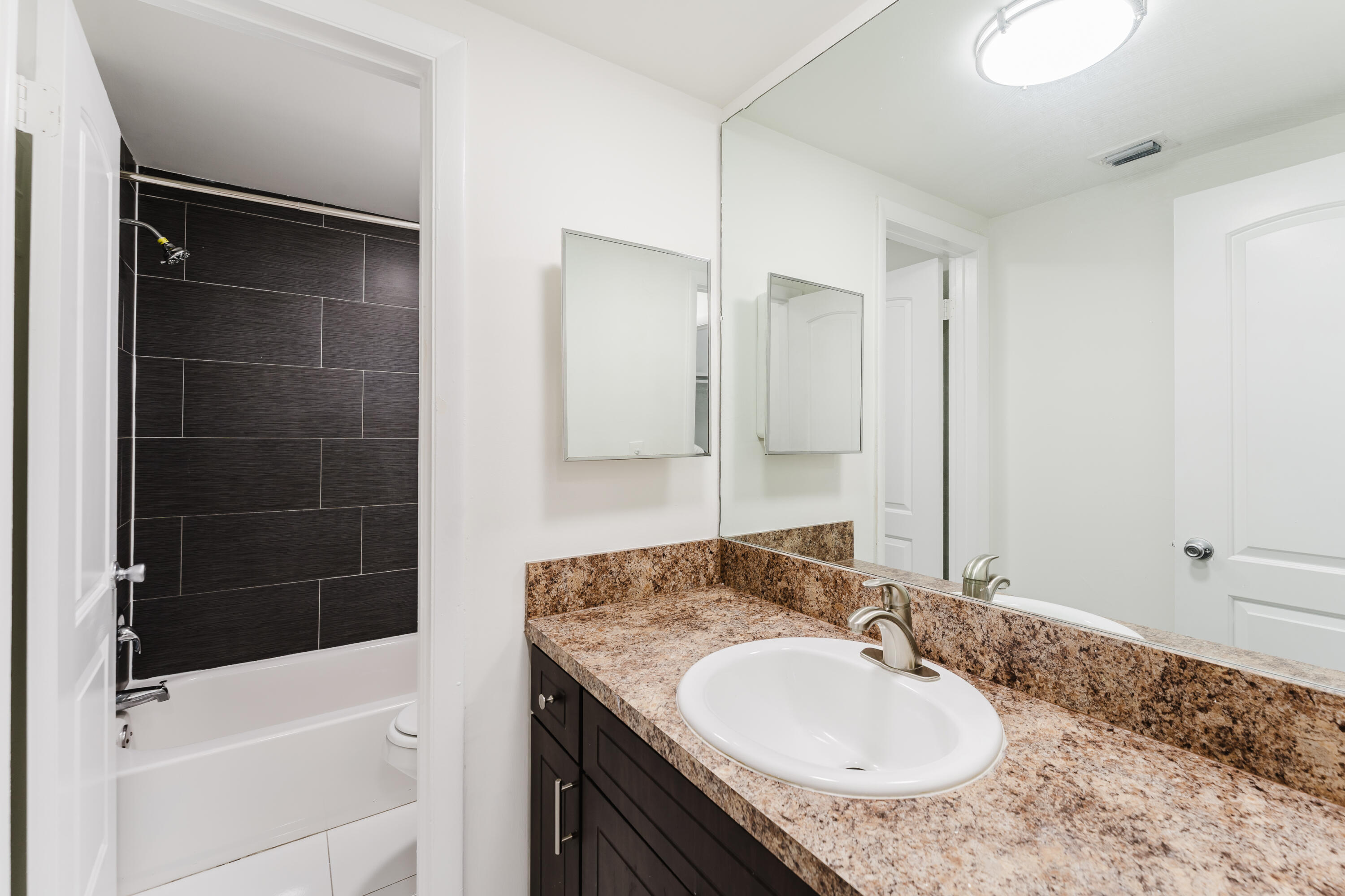 606 Northwest 13th Street, Unit 23 Boca Raton, FL 33486 - Photo 29 of 37 a bathroom with a granite countertop sink a mirror and a bathtub