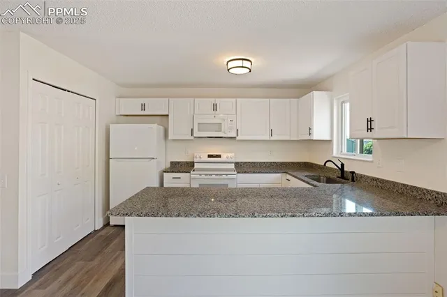 a kitchen with granite countertop a refrigerator a stove and white cabinets