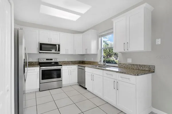a kitchen with granite countertop white cabinets stainless steel appliances and a window