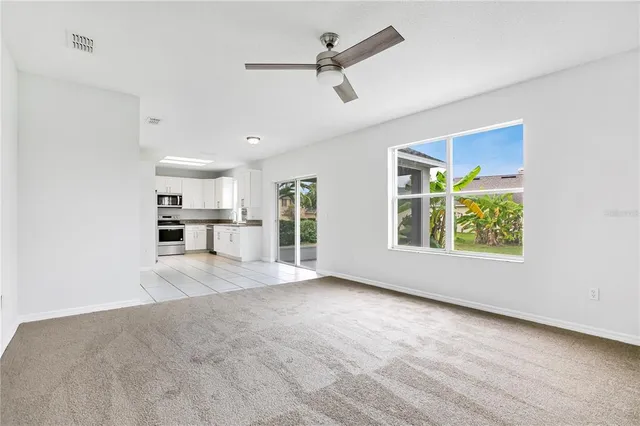 a view of an empty room with a window and kitchen view