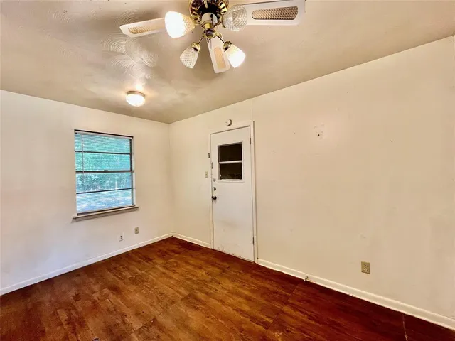 an empty room with wooden floor fan and windows