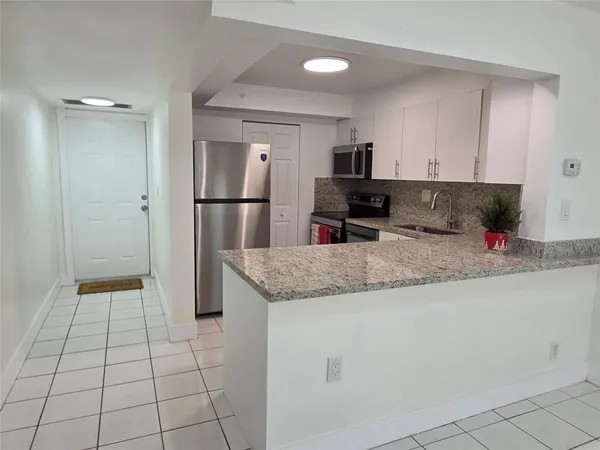 a kitchen with granite countertop a refrigerator a sink and white cabinets