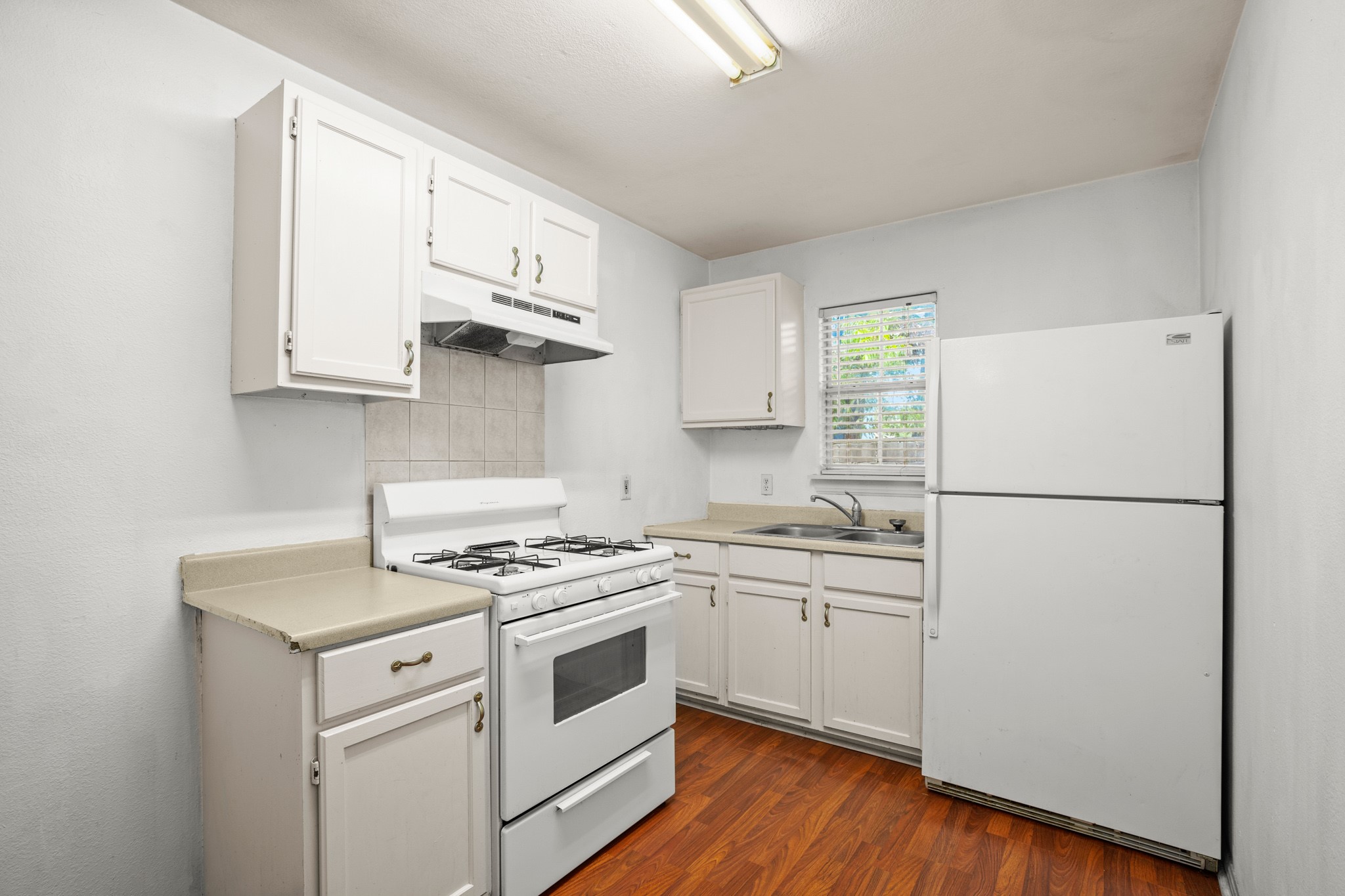 2610 East 3rd Street, Unit B Austin, TX 78702 - Photo 1 of 1 Kitchen featuring white appliances, light countertops, white cabinetry, dark wood-type flooring, and decorative backsplash