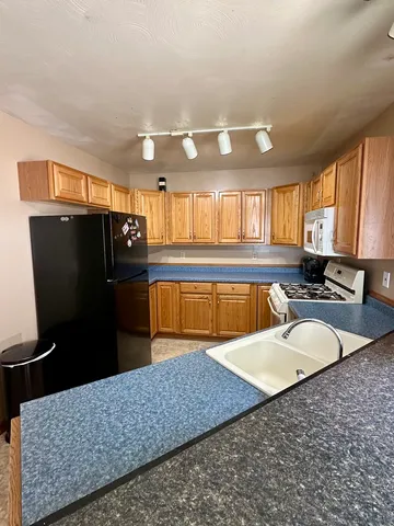 a large kitchen with stainless steel appliances kitchen island granite countertop a refrigerator and a sink