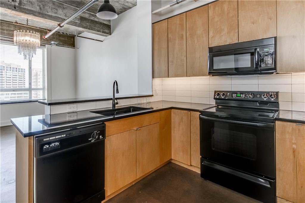 710 Colorado Street, Unit G9 Austin, TX 78701 - Photo 6 of 25 Black appliances and rich countertops equip this modern kitchen with minimalist cabinetry and industrial-inspired ceilings.