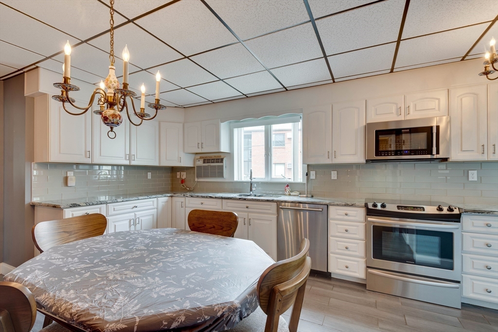 45 Jackson Road Somerville, MA 02145 - Photo 12 of 27 a kitchen with stainless steel appliances granite countertop a sink a stove a microwave oven a refrigerator with grey cabinets and wooden floor