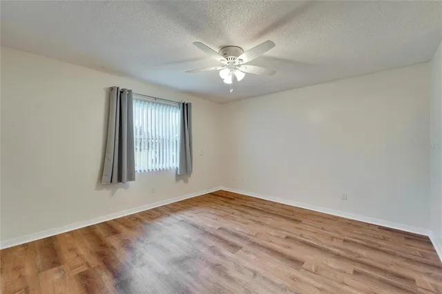 an empty room with wooden floor fan and windows