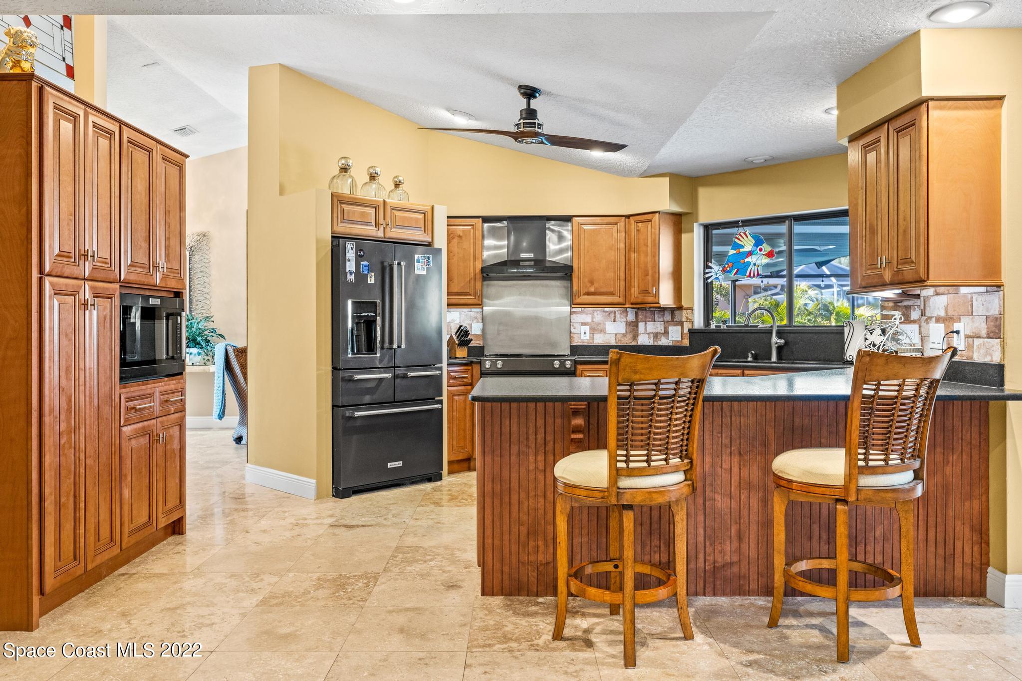 470 Veracruz Boulevard Indialantic, FL 32903 - Photo 6 of 25 a kitchen with stainless steel appliances kitchen island granite countertop a refrigerator a stove a dining table and chairs with wooden floor
