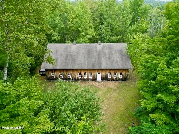 an aerial view of a house with yard and trees in the background