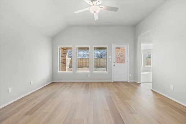 an empty room with wooden floor ceiling fan and windows
