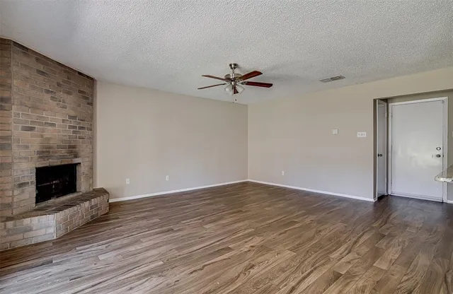 an empty room with wooden floor a chandelier fan and a fireplace