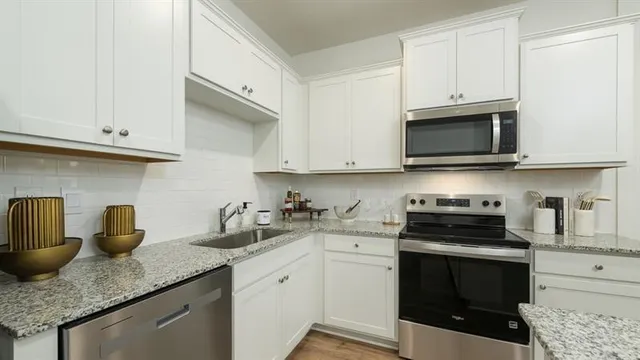 a kitchen with stainless steel appliances granite countertop white cabinets and a stove top oven