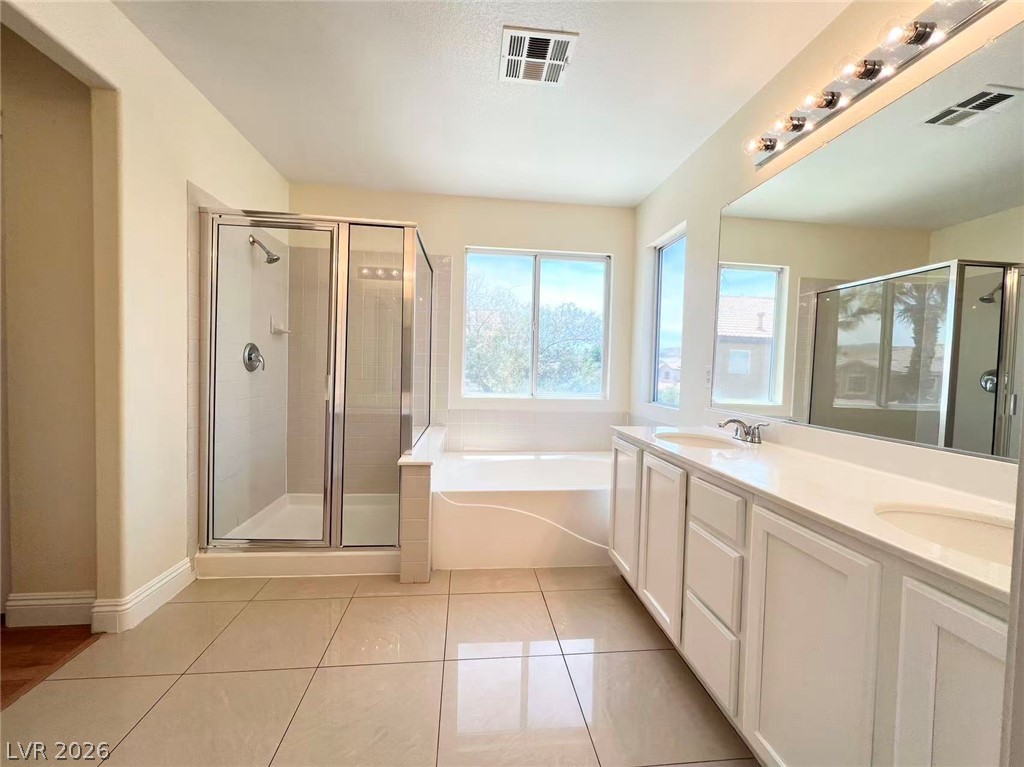 9891 Ridge Hill Avenue Las Vegas, NV 89147 - Photo 18 of 29 A well-lit primary bathroom featuring a spacious walk-in shower and a built-in soaking tub beneath broad windows.
