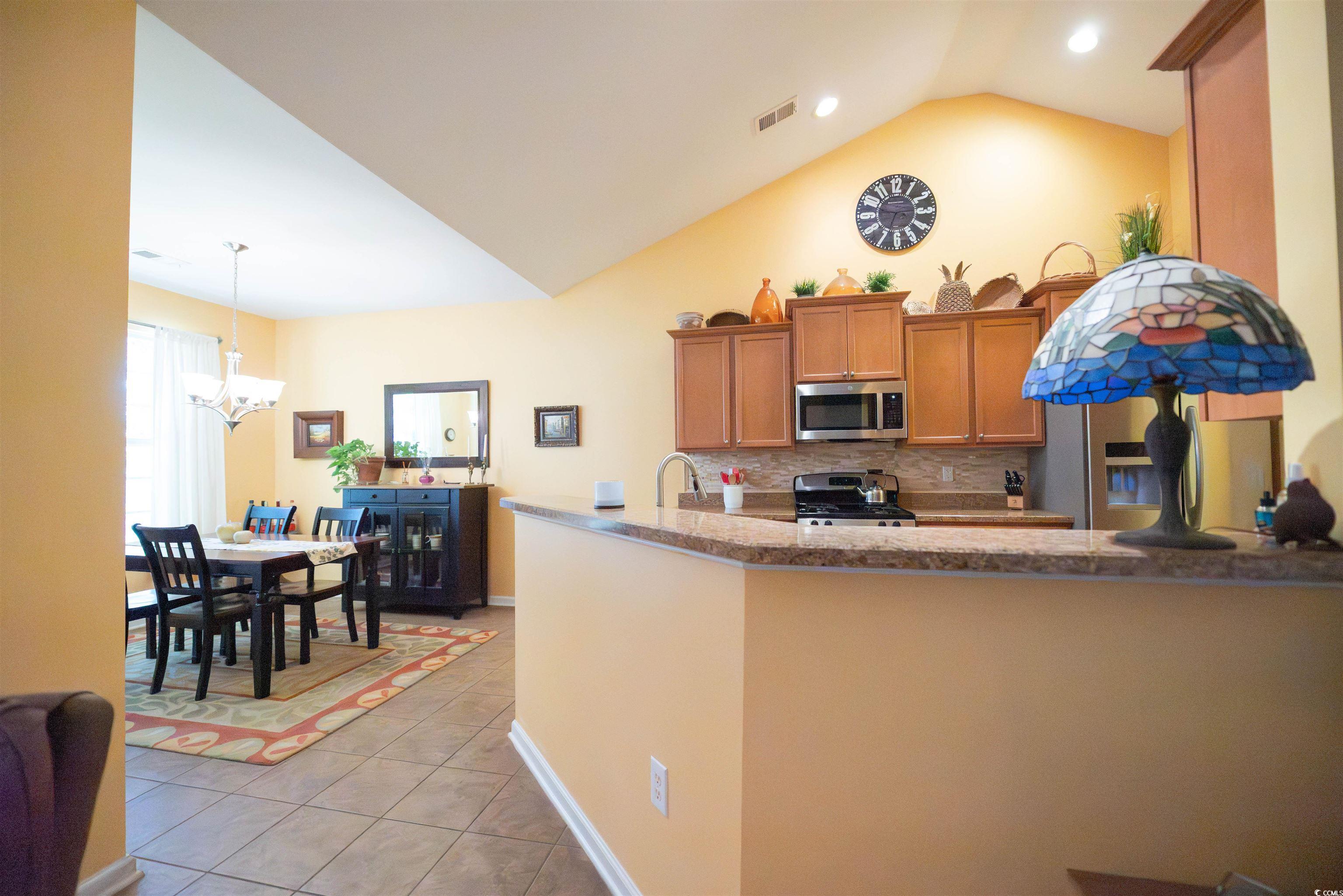 209 Golden Oaks Drive Murrells Inlet, SC 29576 - Photo 13 of 40 Kitchen featuring brown cabinetry, decorative backsplash, stainless steel appliances, light tile patterned flooring, and pendant lighting