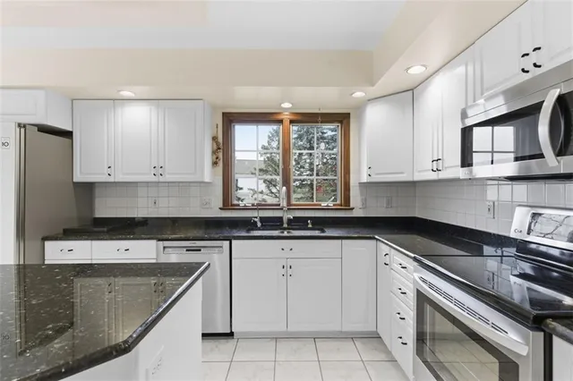 a kitchen with granite countertop white cabinets stainless steel appliances a sink and a window