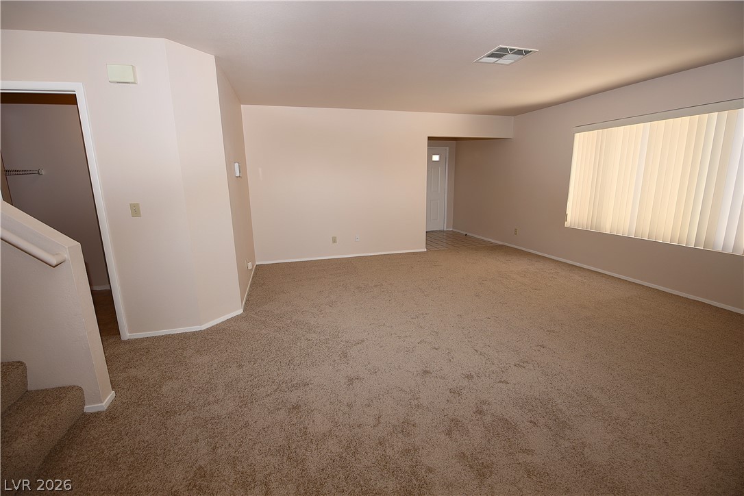 8220 Maplestar Road Las Vegas, NV 89128 - Photo 6 of 29 Well-lit living area features neutral carpeting and a wide window with vertical blinds.