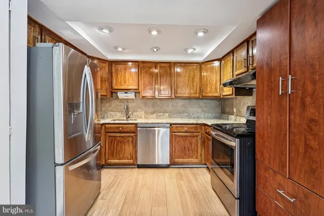 a kitchen with stainless steel appliances granite countertop a refrigerator a sink dishwasher a stove and white countertops with wooden floor