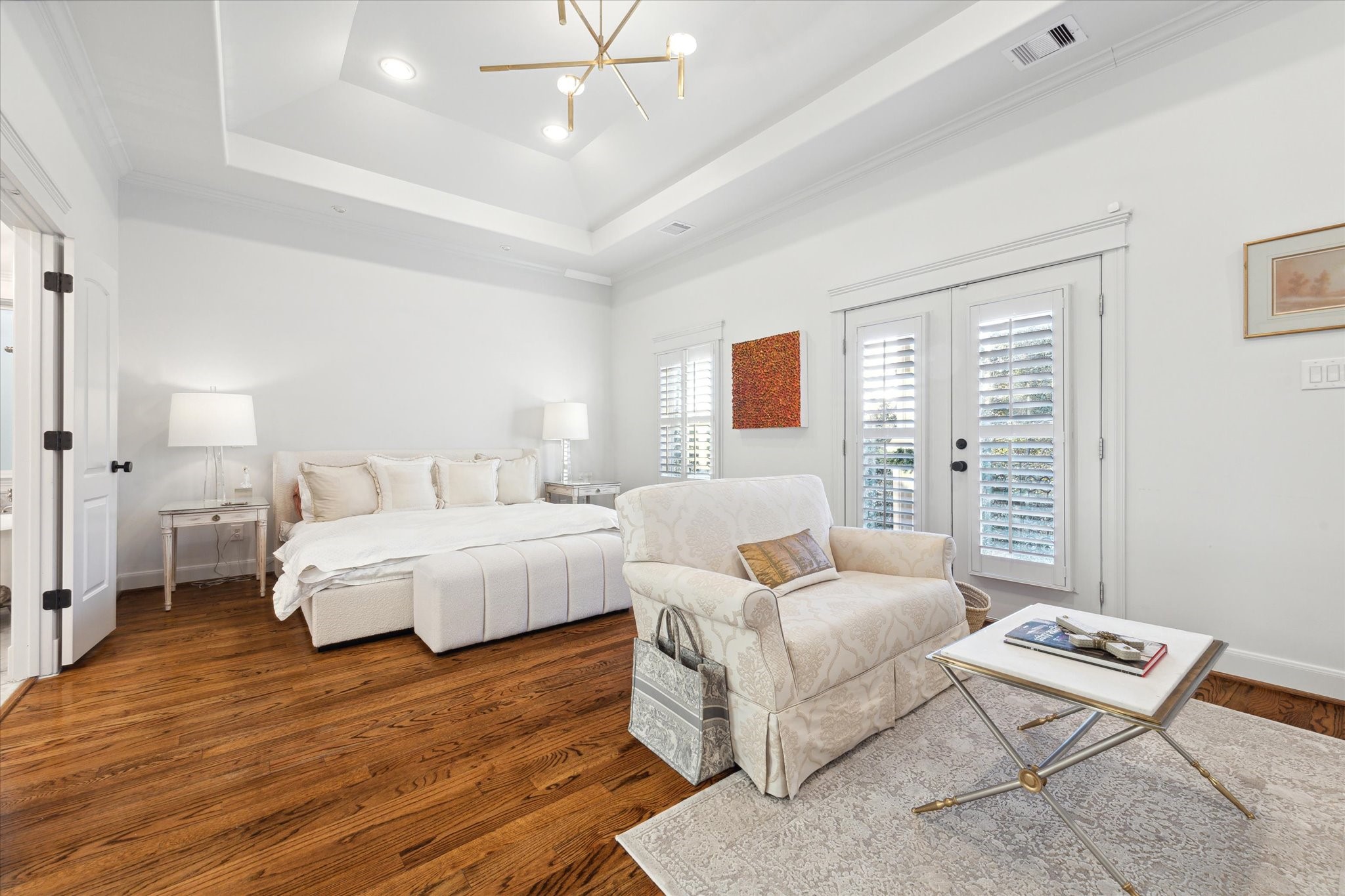606 Rutland Street Houston, TX 77007 - Photo 32 of 48 The primary bedroom features a cozy sitting area and desk, elegant hardwood floors, and abundant natural light from French doors with plantation shutters. The room is tastefully decorated with neutral tones and modern lighting, creating a serene and inviting atmosphere.