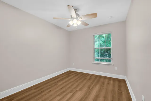 an empty room with wooden floor fan and windows