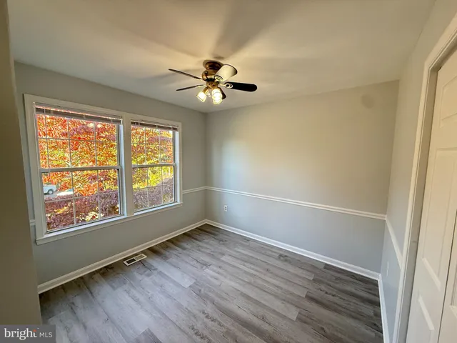 an empty room with wooden floor fan and windows